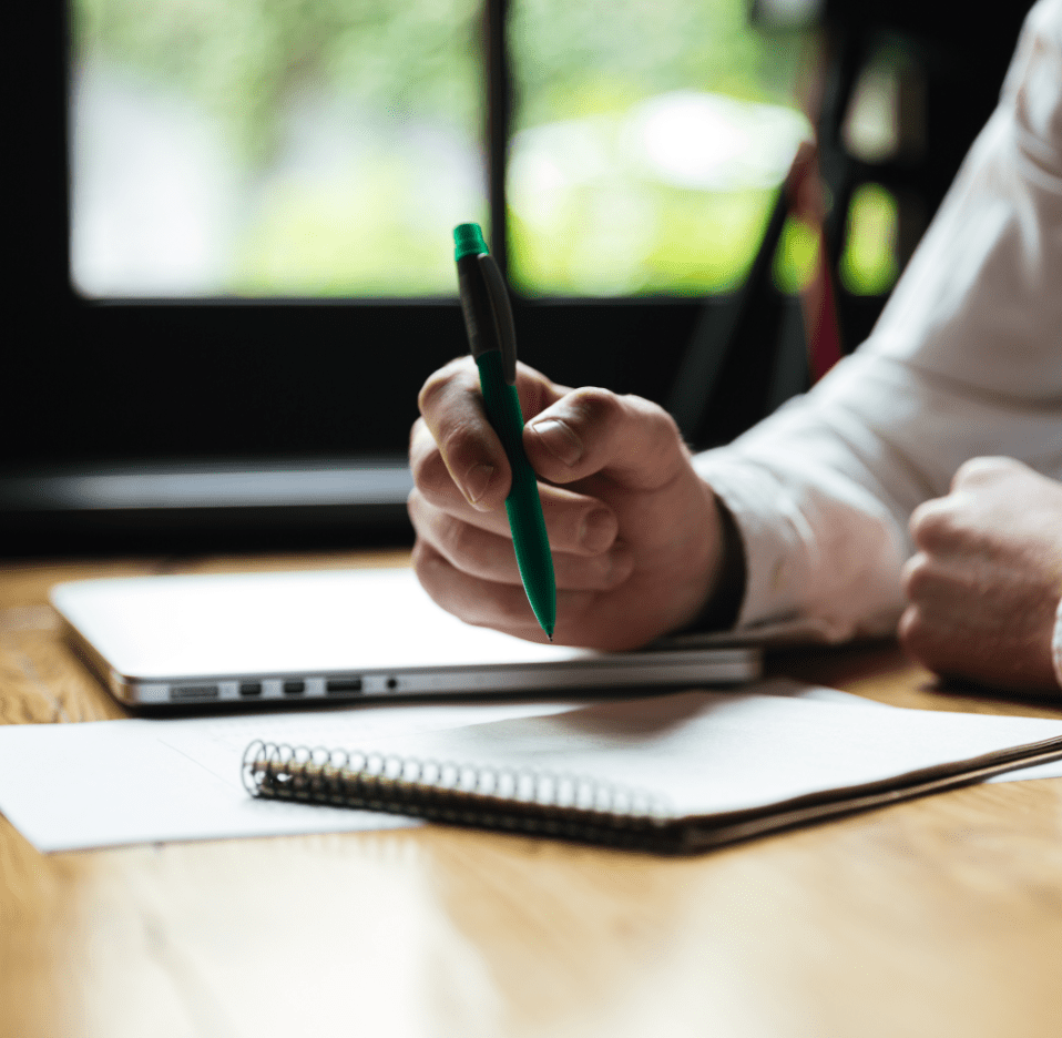 cropped-photo-mans-hand-holding-green-pen-while-taking-notes